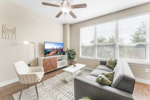 A modern living room with a sofa, a coffee table, a TV, and a ceiling fan. - Fun Soco 1BR King Suite w Gympickleballlaundry (Austin)