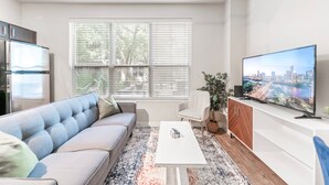 A modern living room with a sofa, coffee table, TV, and a cityscape view. - Comfy Soco 1BR King Suite w Gympickleballlaundry (Austin)