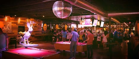 A bar area with pool tables, a disco ball, and a crowd of people.
