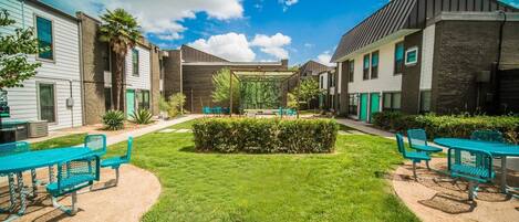 A courtyard with green grass, a central garden, and outdoor seating with chairs and tables.
