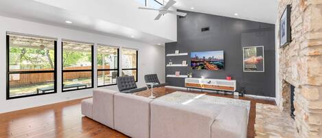 A spacious living room with a large sectional sofa, a flat-screen TV mounted on a dark wall, and a stone fireplace.