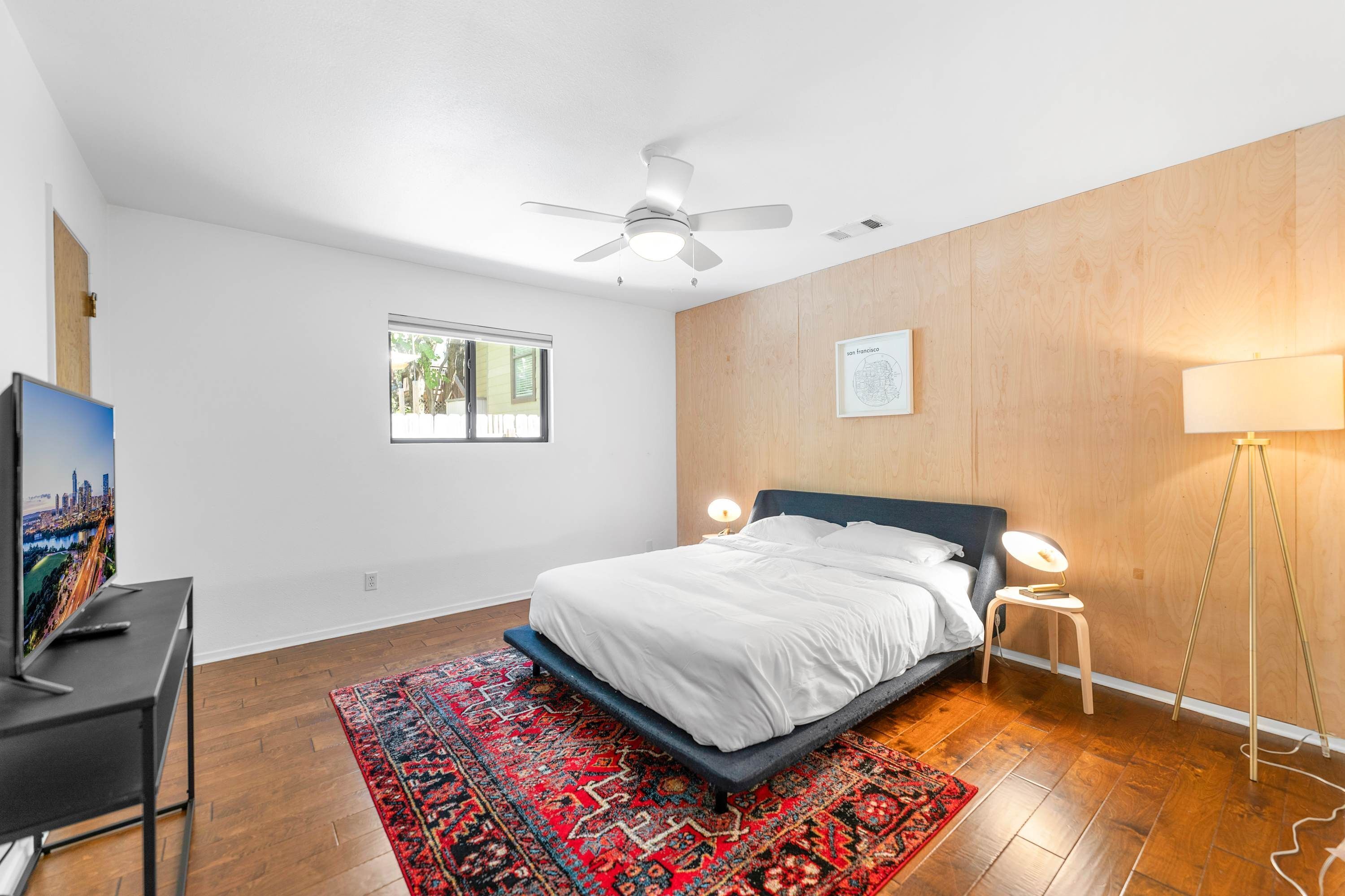 Ein Schlafzimmer mit einem Bett, einem Schreibtisch mit Fernseher, einer Stehlampe und einem Deckenventilator.