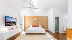 A modern bedroom with a bed, a TV, a ceiling fan, and a wooden accent wall. - Close to Domain DT Shopping Chic Serene 3BR (Austin)