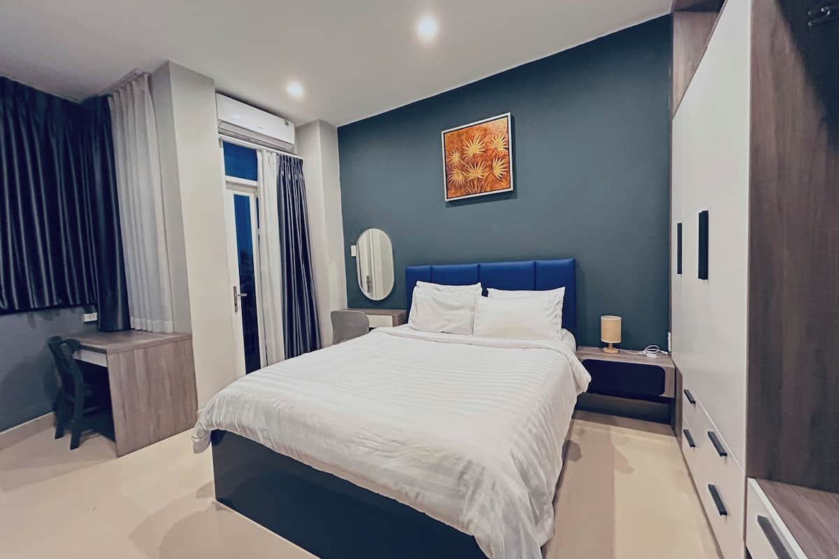 A modern bedroom with a large bed, a desk, and a wardrobe.