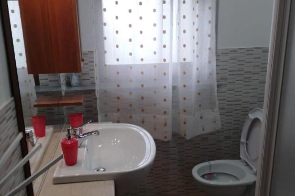 Ein Badezimmer mit einem weißen Waschbecken, roten Tassen, einer Toilette und einem Duschvorhang mit Punkten.