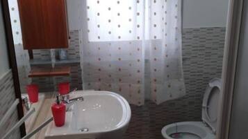Ein Badezimmer mit einem weißen Waschbecken, roten Tassen, einer Toilette und einem Duschvorhang mit Punkten.