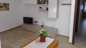 A modern living room with a flat-screen TV, a wooden coffee table, and a potted plant.