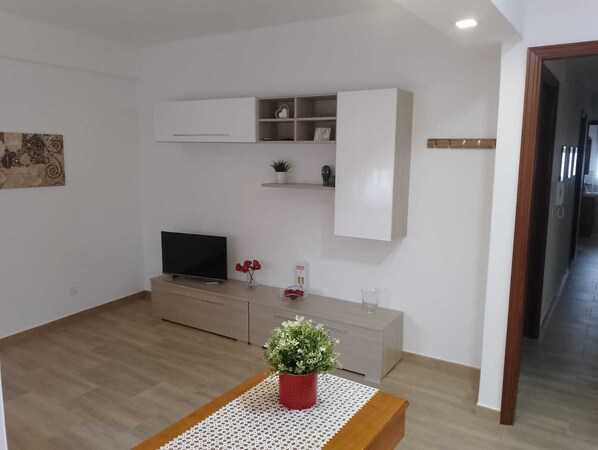 Una sala moderna con un televisor de pantalla plana, una mesa de centro de madera y una planta en maceta.