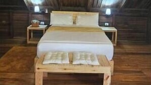 A wooden ceiling in a room with a bed, two bedside tables, and a fur rug on the floor.