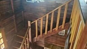 A wooden staircase in a rustic attic room with a hanging light fixture.