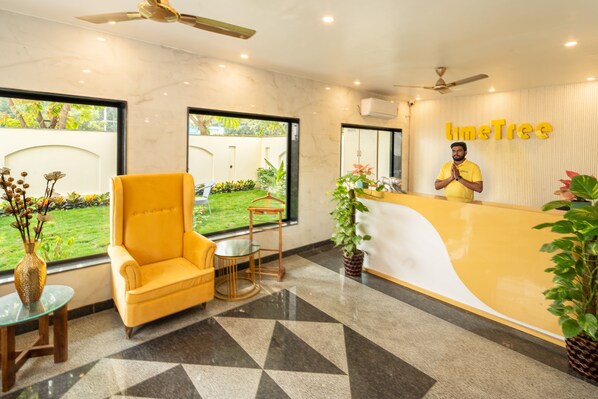 Zona de recepción con un sofá amarillo, un mostrador de recepción y vistas a un jardín.