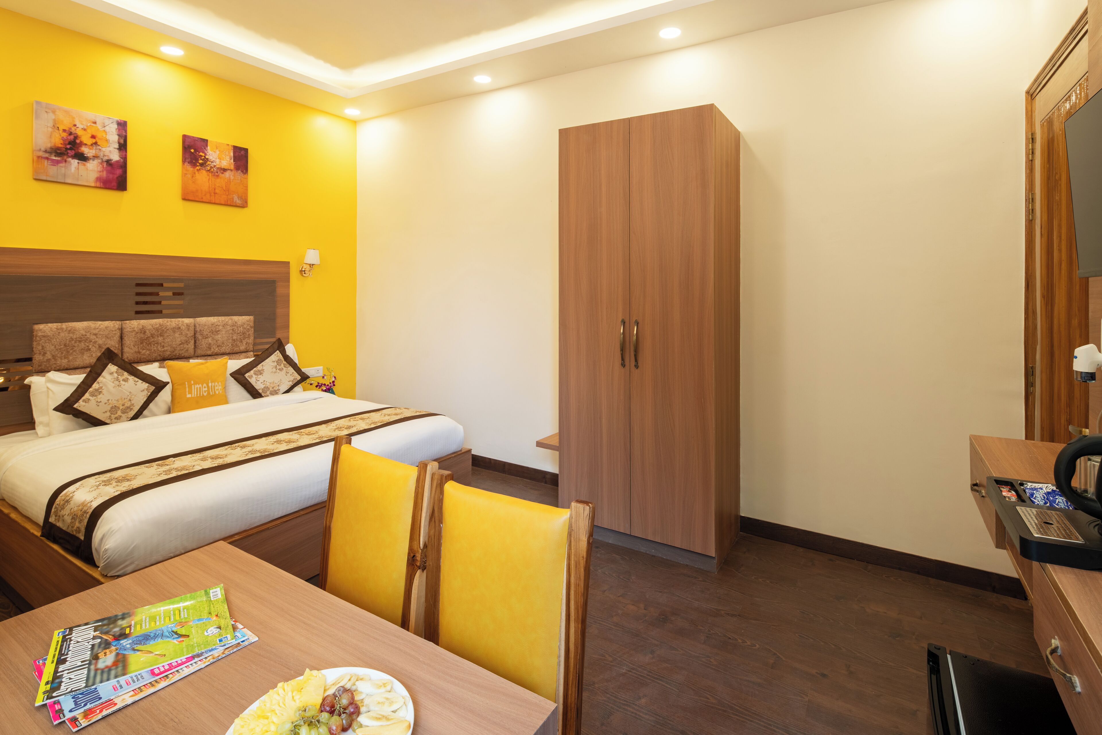 A hotel room with a bed, a wooden wardrobe, a desk with a telephone, and a dining table with a magazine and a plate of food.