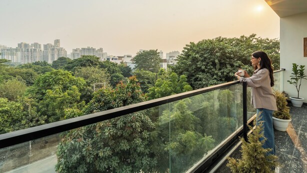 A balcony with a glass railing overlooking a cityscape and lush greenery. - Lime Tree Hotel & One BHK Serviced Apartment - Noida Sector 50 Metro (Noida)