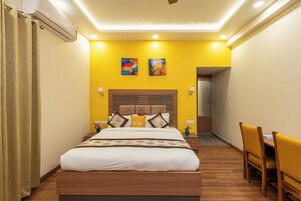 Hotelkamer met een groot bed, een houten hoofdbord, twee schilderijen aan de muur, een klein tafeltje met stoelen en een airconditioner.