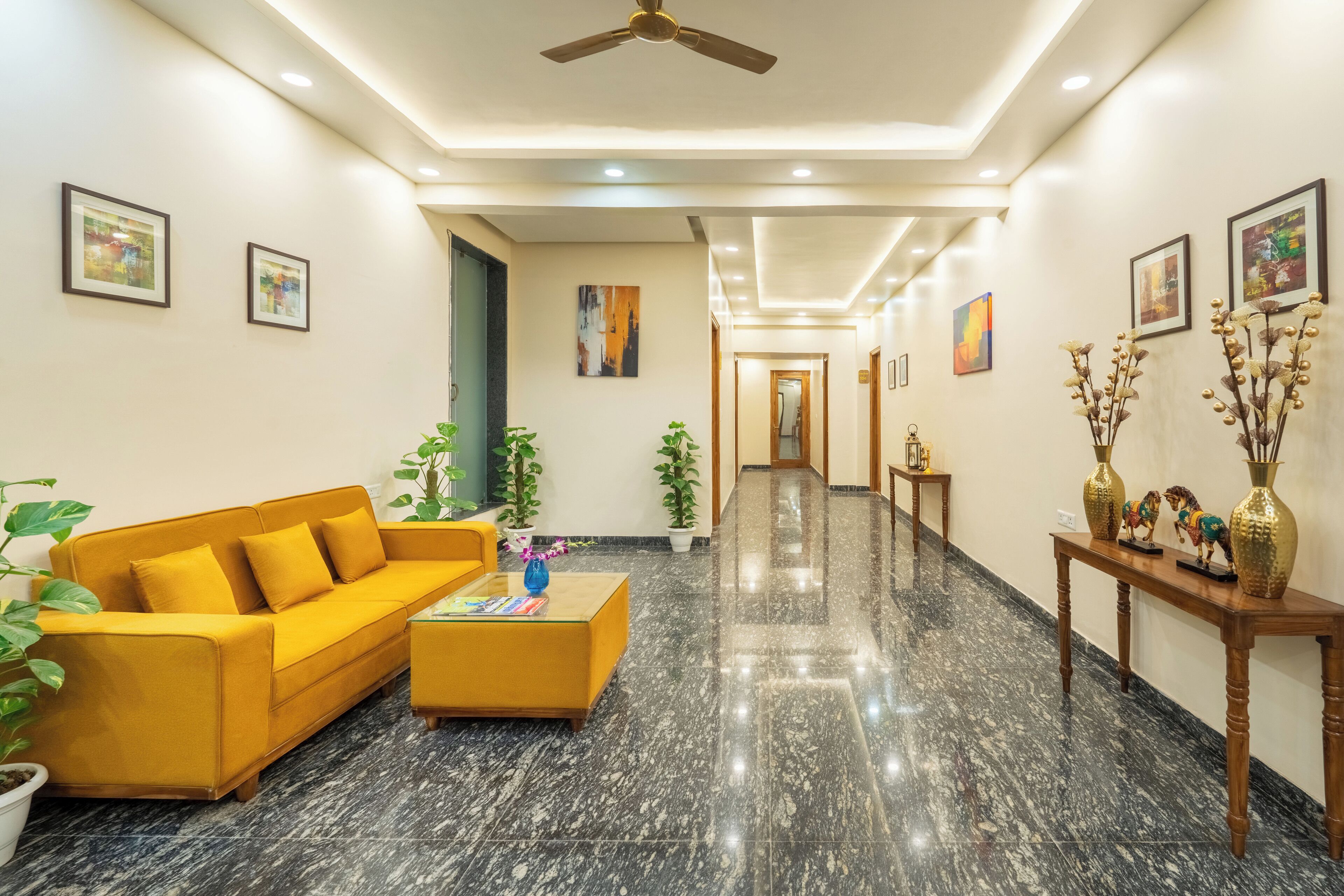 Una hall d'albergo moderna con un divano giallo, un tavolino da caffè, piante in vaso e quadri alle pareti.