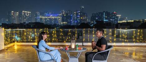 Two people seated at a round table with a city skyline in the background.