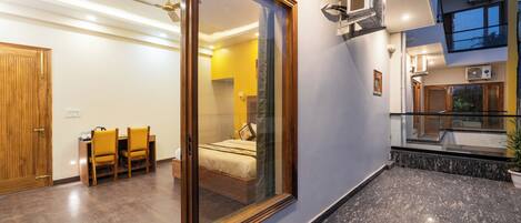 A modern hotel room with a sliding glass door leading to a balcony, a wooden dining table with chairs, and a bed with a nightstand.