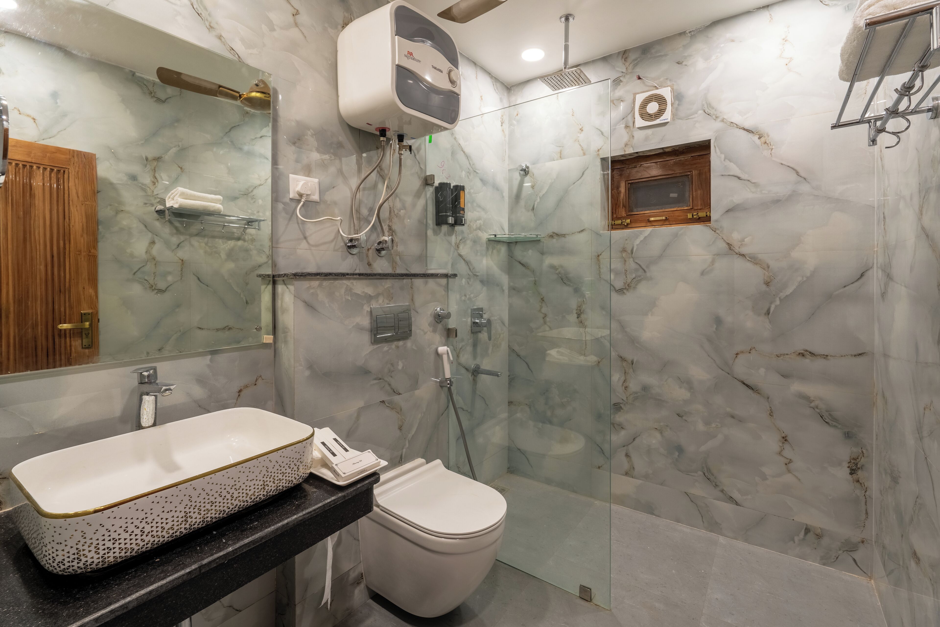 Un baño con pared de mármol, un lavabo blanco, un inodoro y zona de ducha con mampara de vidrio.