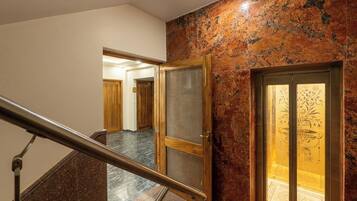 A marble staircase with a metal handrail, leading to a room with a wooden door and a decorative glass panel.