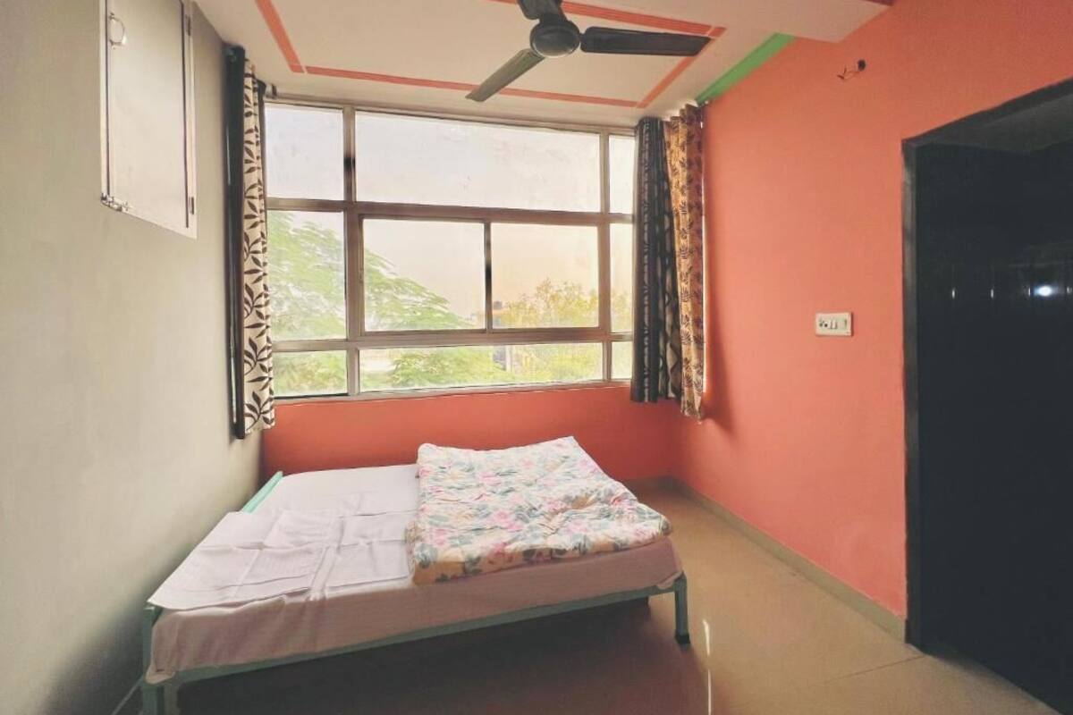 A room with a bed, a ceiling fan, a window with curtains, and a door.