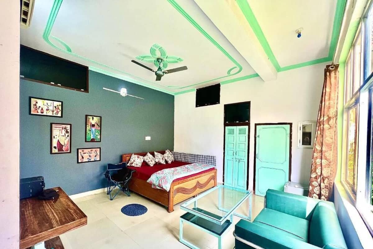 A bedroom with a bed, a desk, a chair, a sofa, a ceiling fan, and a window with curtains.