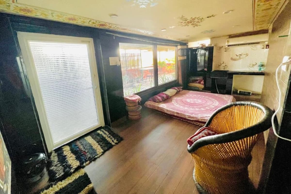 A room with a bed, a wicker chair, a television, and a window with blinds.