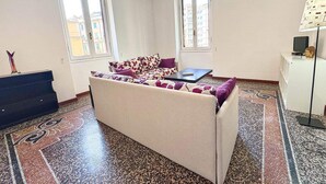 A room with a sofa, a small table, a lamp, and a decorative item on a cabinet. - LIVE YOUR STAY (Genova)
