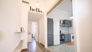 A hallway leading to a kitchen with a 'hello.' sign, a washing machine, and a patterned floor. - LIVE YOUR STAY (Genova)