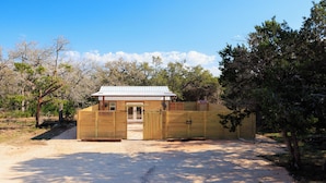 A small wooden building with a metal roof, surrounded by trees and a gravel path.