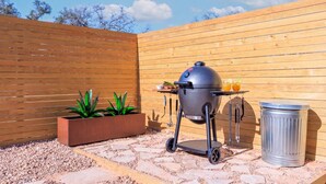 Ein Grill mit Wagen, ein Mülleimer und ein Pflanzgefäß mit Grünpflanzen.
