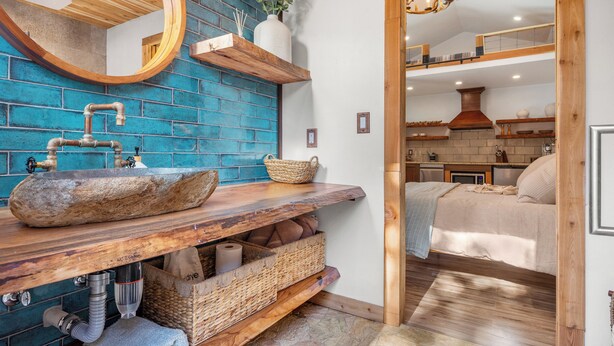 A bathroom with a large stone sink, wooden shelves, and a blue tiled wall.