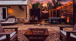 A rustic outdoor seating area with a fire pit labeled 'BENGALA,' a wooden building with a sign 'AVANDARD RANCH,' and a wooden fence with string lights.