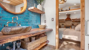 Een badkamer met een stenen wastafel, een houten opbergmeubel en een blauwe baksteenmuur.