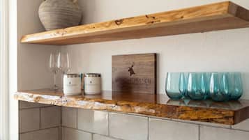 Un comptoir de cuisine avec une étagère en bois, deux récipients, une enseigne en bois et quatre verres.