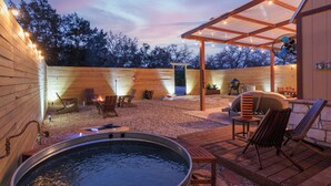 A wooden deck with a hot tub, outdoor seating, and a pergola with string lights.