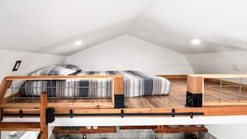 A loft bedroom with a sloped ceiling, a bed with striped bedding, and a kitchen area below.