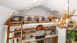 A loft-style bedroom with a bunk bed, a wooden ladder, and a chandelier.