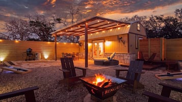 Un patio al aire libre acogedor con un brasero, asientos y un área cubierta con guirnaldas de luces.