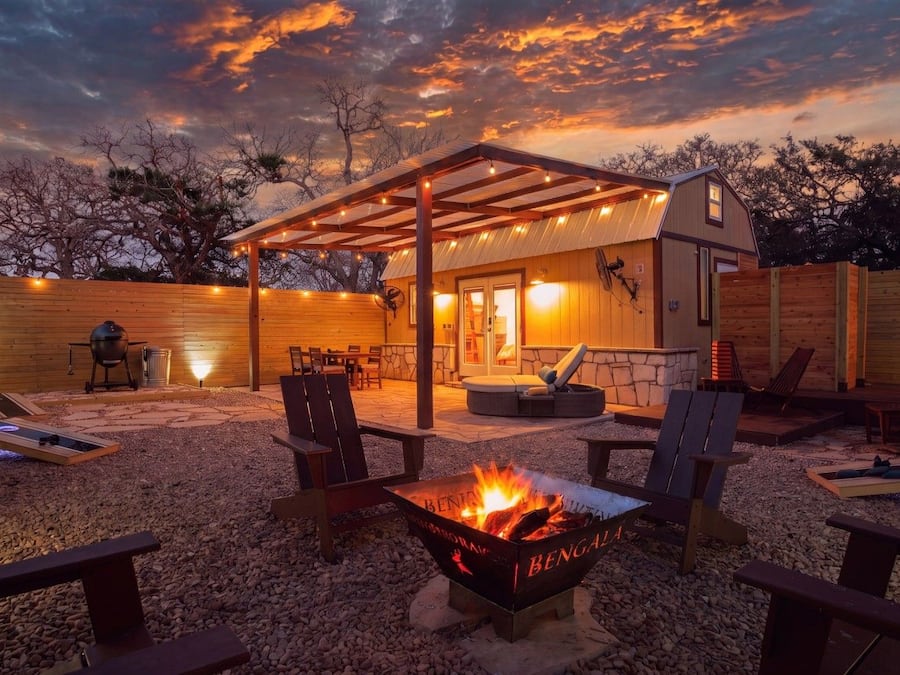 A cozy outdoor patio with a fire pit, seating, and a covered area with string lights.