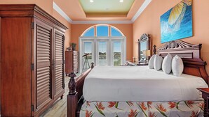 A bedroom with a large bed, wooden wardrobe, and a view of the water through the arched window. - 🏖️🏝️Waterfront-Inlet Beach-Pool & Hot Tub-Red Retreat (Pensacola)