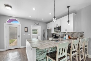 A modern kitchen with white cabinets, a large island, and a stone backsplash.