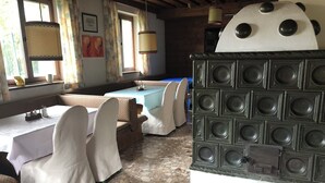 Un comedor con mesas y sillas, una estufa decorativa grande y un ventanal con cortinas.