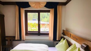 Habitación de hotel con cama doble, ventana con cortinas, radiador y cabecera de madera con placa.