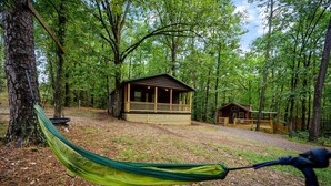 A cabin in a forest with a hammock in the foreground.