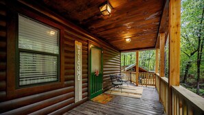 A wooden cabin with a porch, a welcome sign, and a view of the forest.
