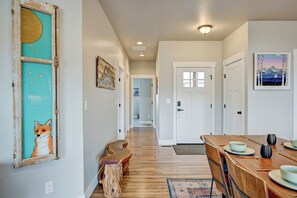 Un pasillo con piso de madera, un comedor con una mesa dispuesta para dos personas y una obra de arte enmarcada en la pared.