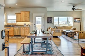 A modern kitchen with wooden cabinets, a dining table with chairs, a sofa, and a ceiling fan.