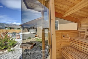 A wooden sauna with benches and a glass door reflecting a mountainous landscape.