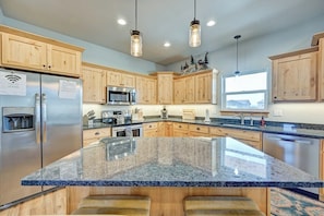 Una cocina moderna con encimeras de granito, electrodomésticos de acero inoxidable, armarios de madera e iluminación colgante.