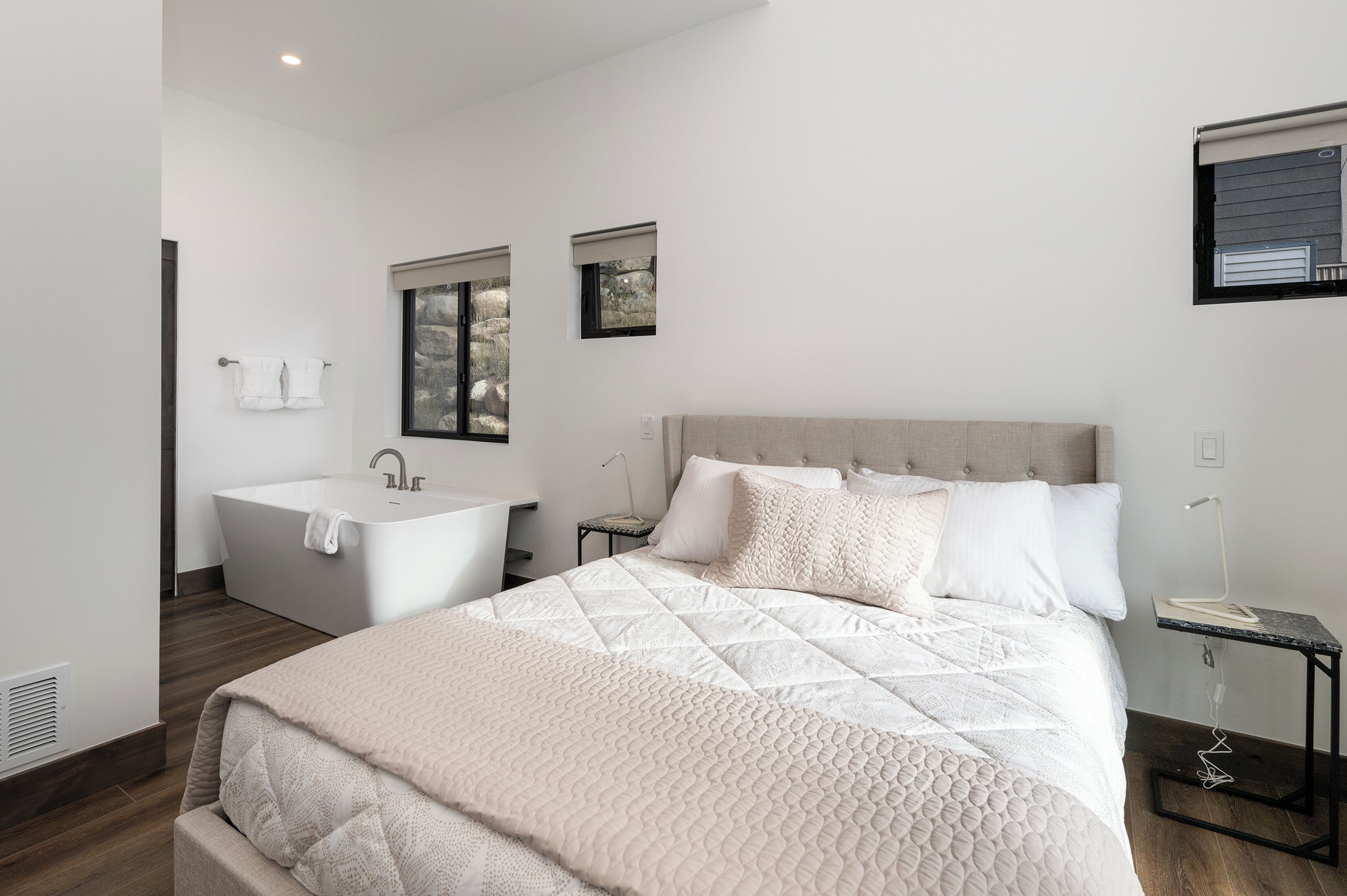 Un dormitorio moderno con una cama grande, una bañera integrada y una mesita de noche pequeña.